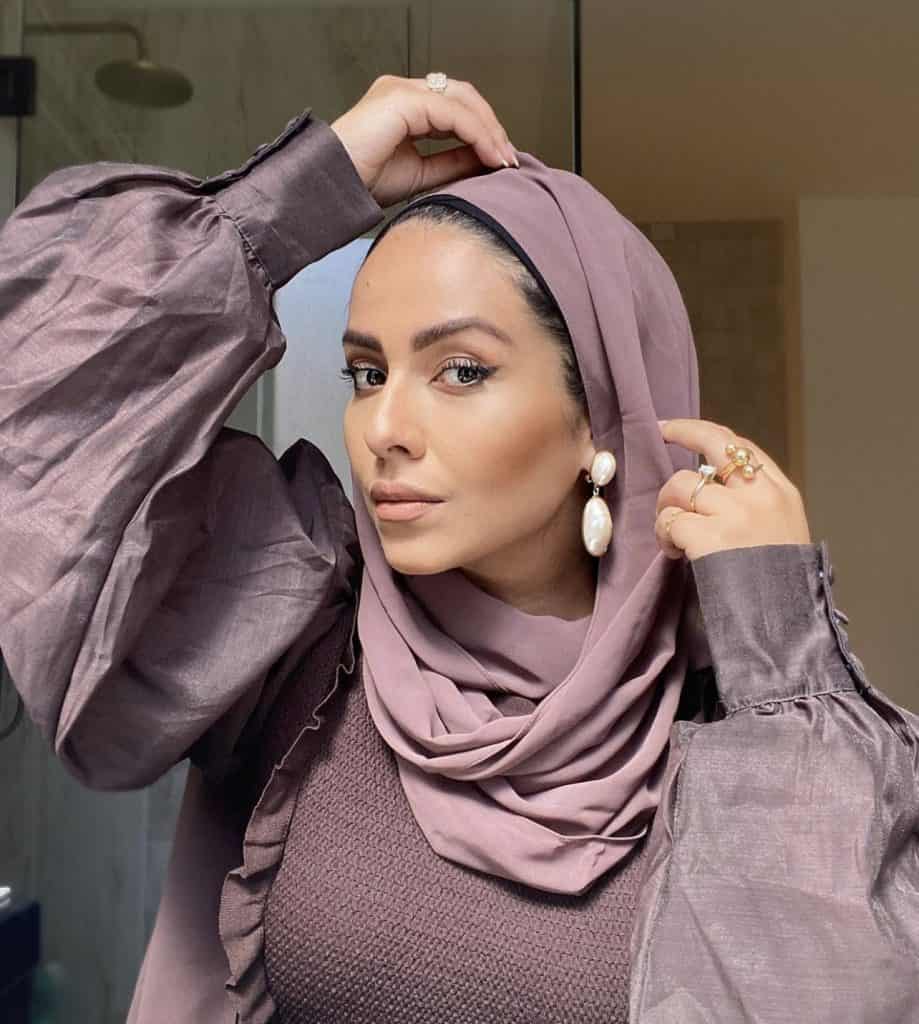 A woman adjusting her purple hijab wearing a purple jacket