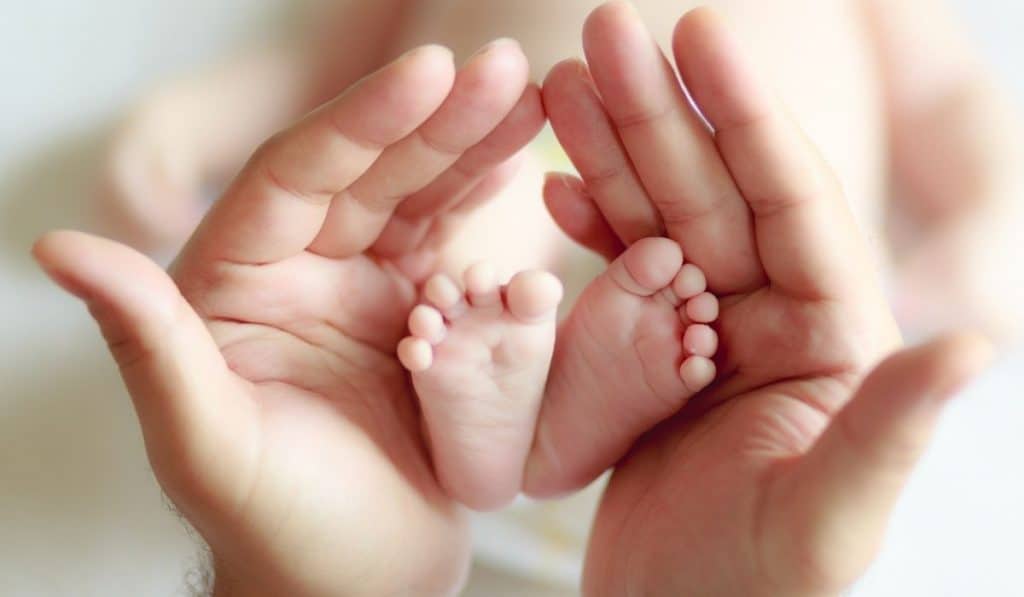 child holding newborn feet between her hands