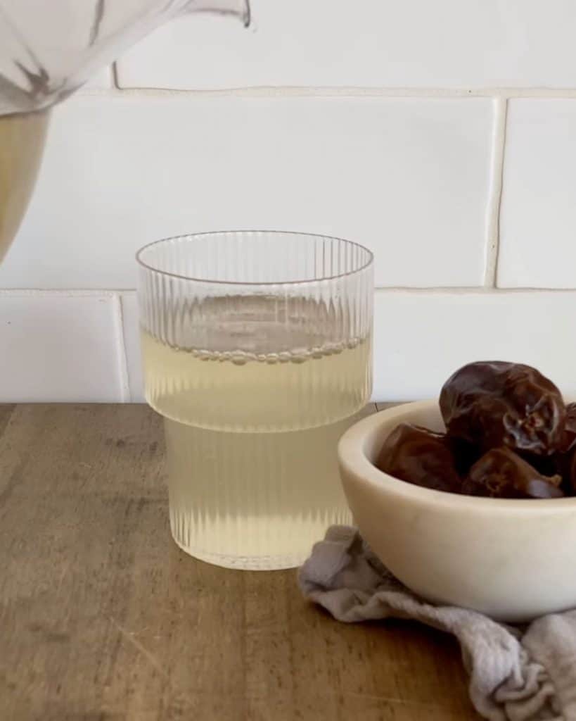 A jug pouring a glass of Nabeez, a prophetic drink made with dates or raisins with a small bowl of dates beside it
